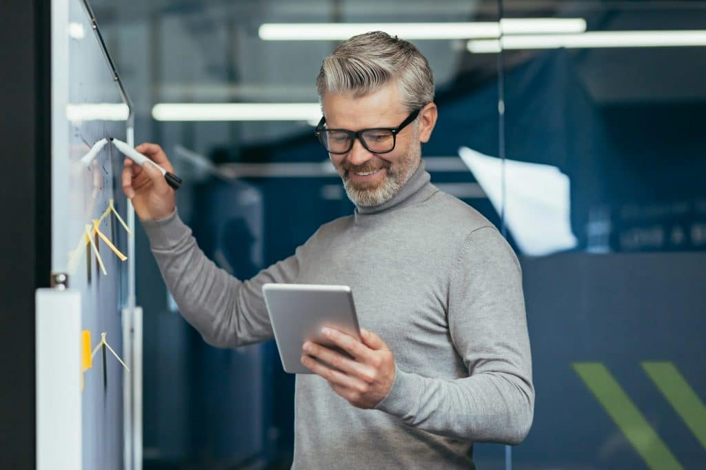 Mature man inside office near whiteboard with colored notes writing down strategy and business plan